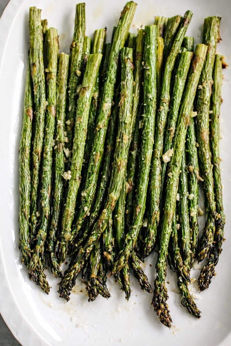 A platter of roasted asparagus spears seasoned with garlic, salt, and pepper, arranged neatly on a white plate.