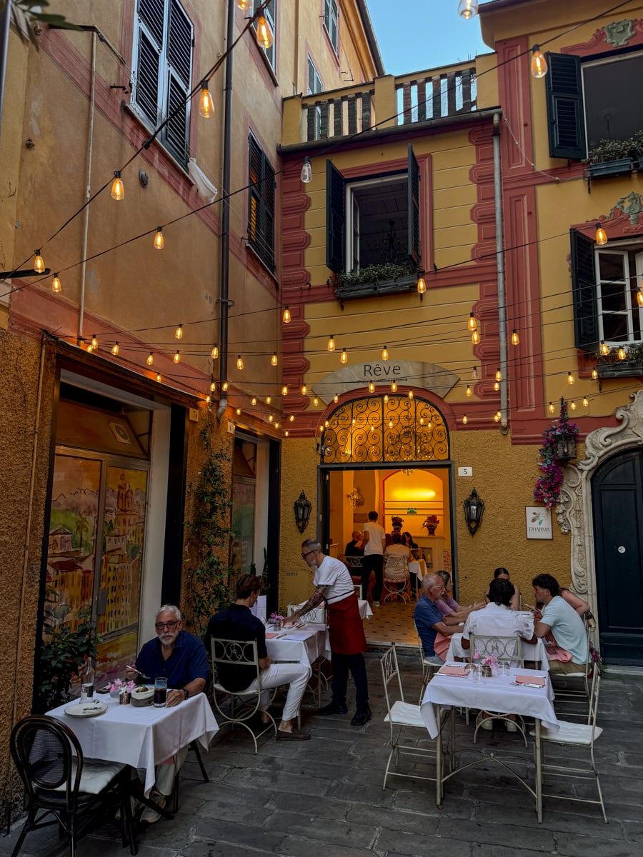 Outdoor restaurant scene in a charming, narrow European alley in Santa Margherita Ligure, with string lights overhead, people dining at white-clothed tables, and warm-colored buildings in the background.