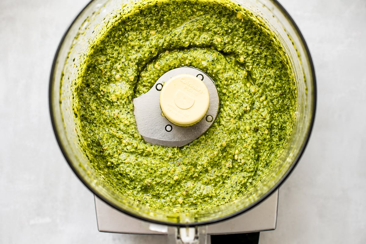 Overhead view of a food processor filled with freshly made green pesto sauce, showing a smooth and slightly textured mixture.