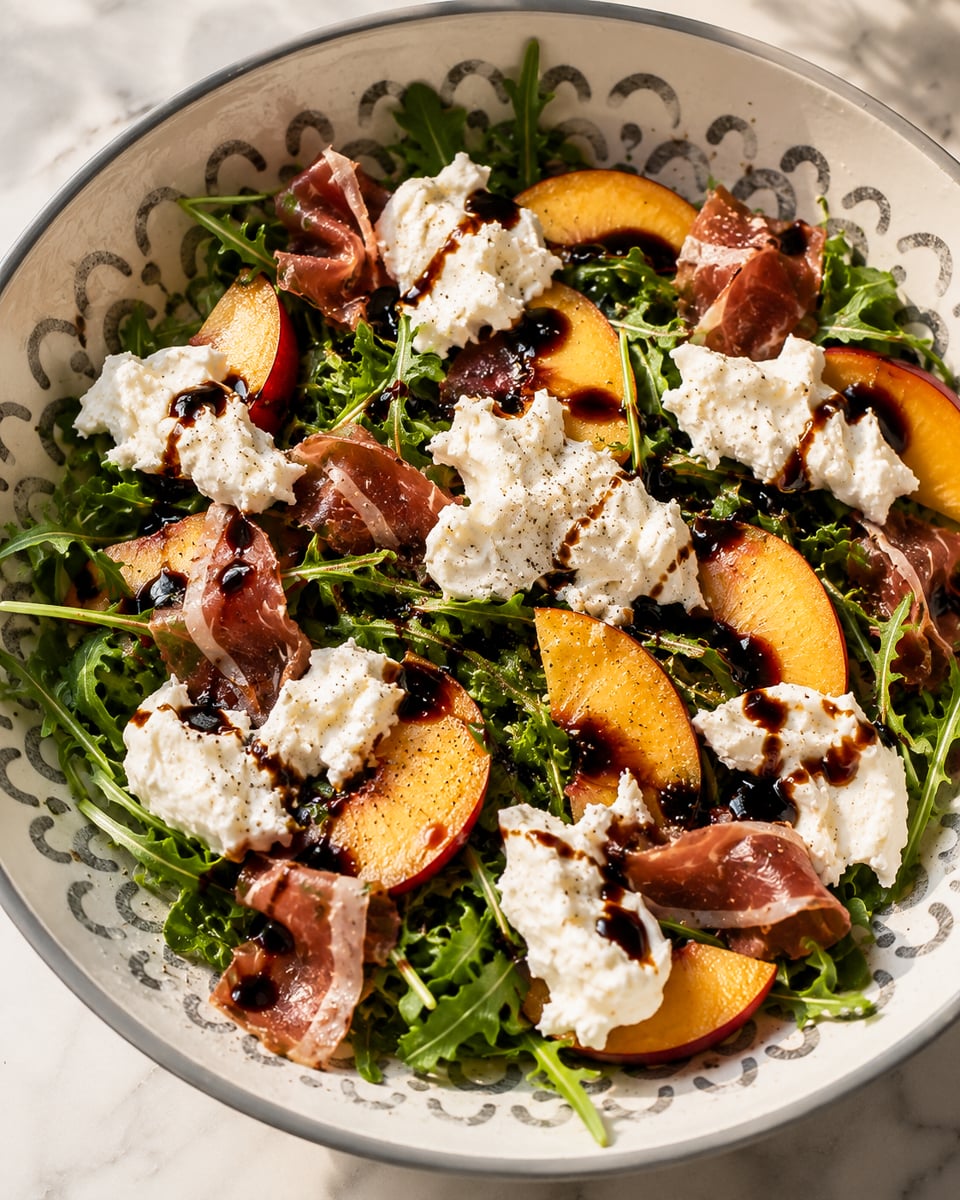 A bowl of arugula salad topped with peach slices, prosciutto, dollops of burrata cheese, and drizzled with balsamic glaze. The salad is arranged in a patterned bowl on a marble surface.