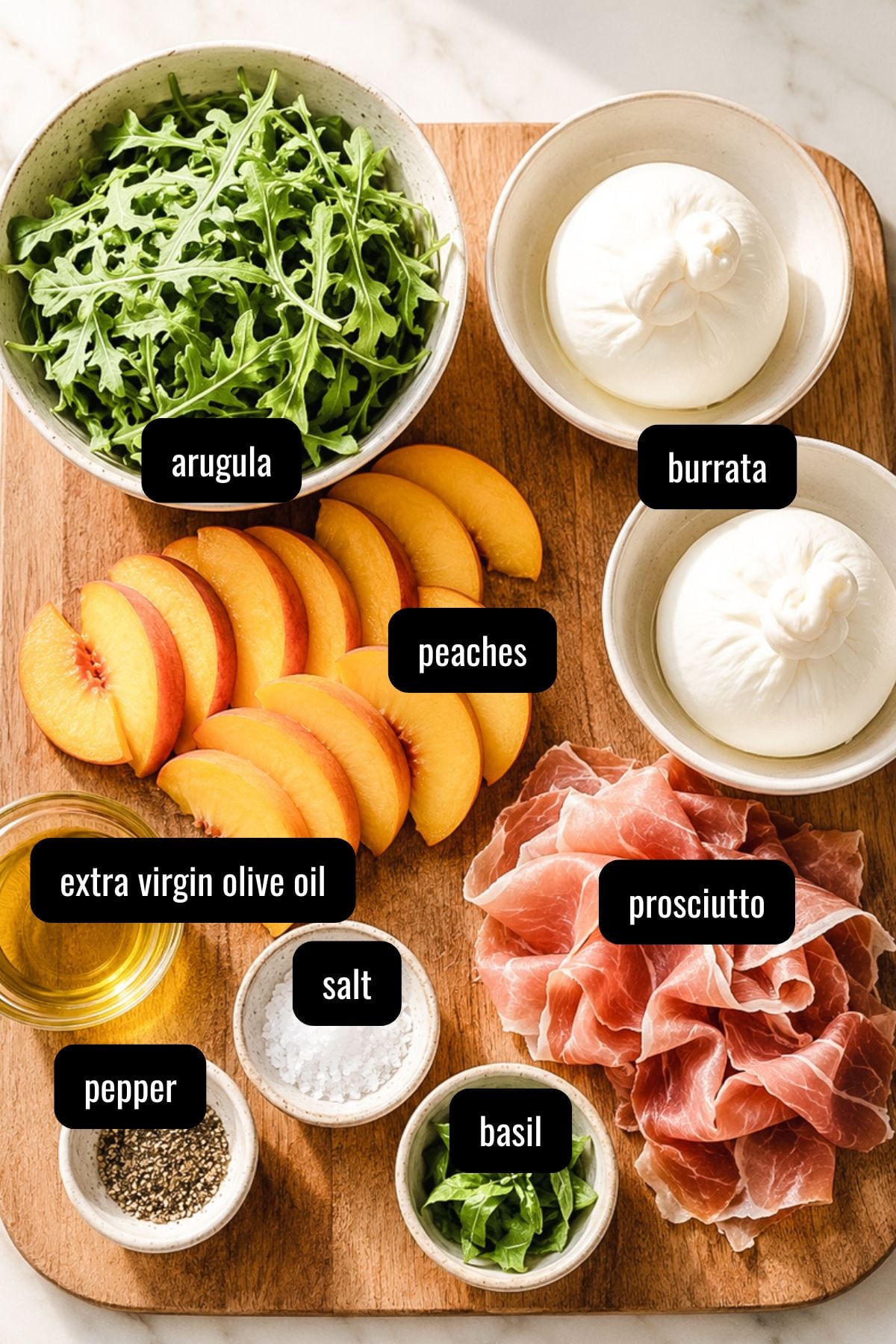 A wooden board with bowls and piles of arugula, burrata, sliced peaches, prosciutto, extra virgin olive oil, salt, pepper, and basil, each ingredient labeled with black text.