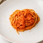 A plate of spaghetti topped with red tomato sauce, garnished with a light sprinkle of grated cheese, on a white plate set against a light background.