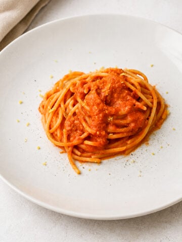A plate of spaghetti topped with red tomato sauce, garnished with a light sprinkle of grated cheese, on a white plate set against a light background.