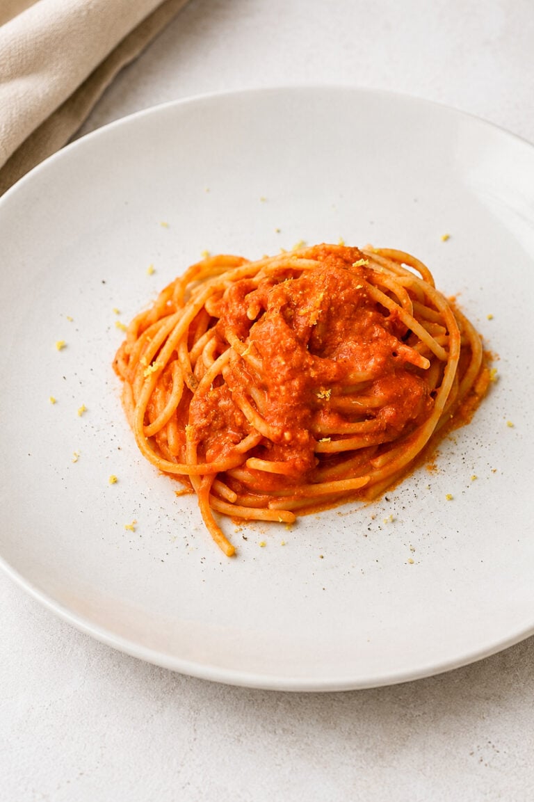 A plate of spaghetti topped with red tomato sauce, garnished with a light sprinkle of grated cheese, on a white plate set against a light background.