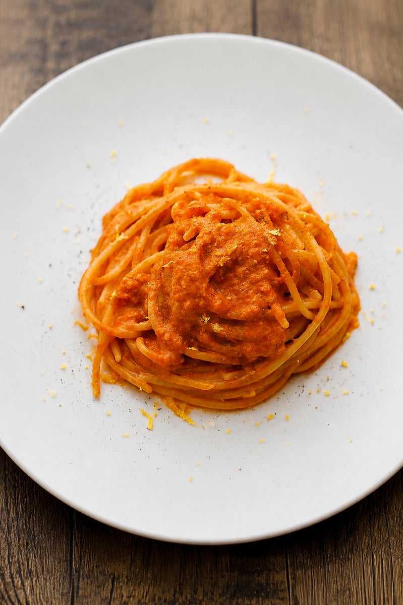 A neatly twirled serving of spaghetti topped with a thick orange-red tomato sauce sits on a white plate, placed on a wooden table.