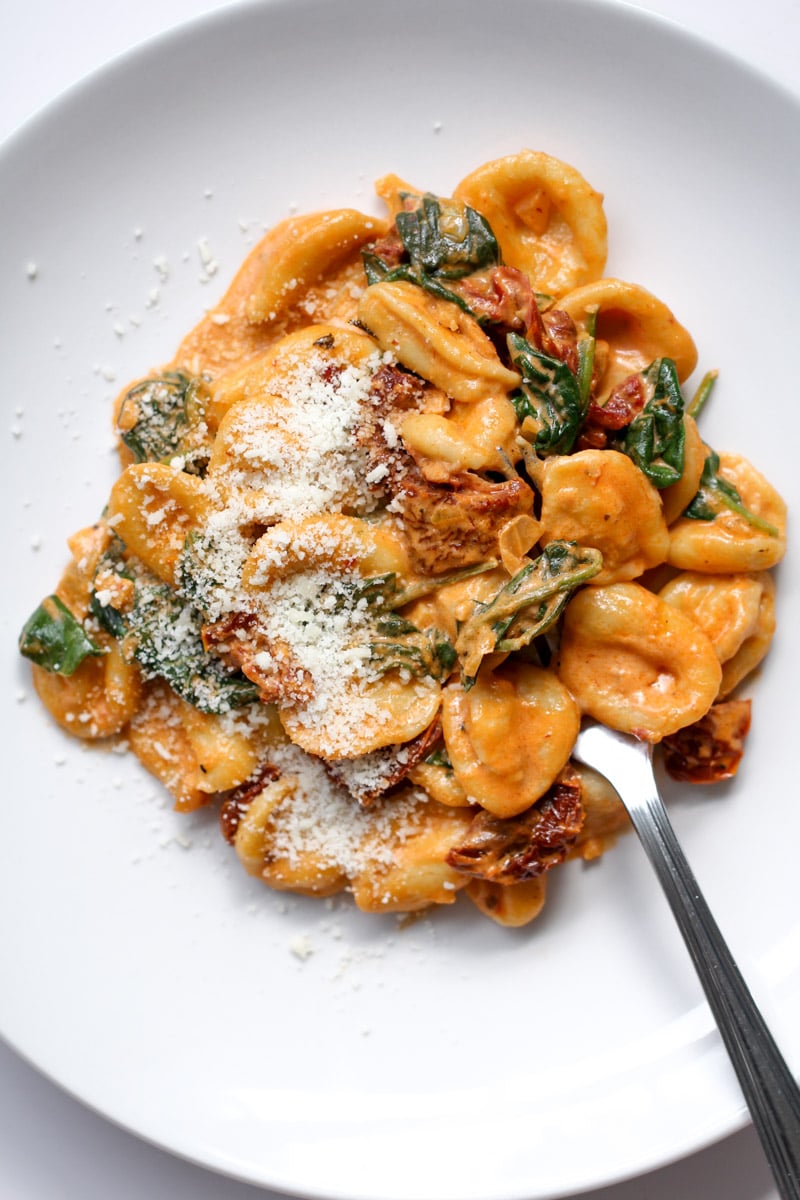 Orecchiette pasta with creamy tomato sauce, spinach, sun-dried tomatoes, and grated parmesan, served on a white plate with a fork.