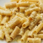 A plate of rigatoni pasta covered in creamy cheese sauce, topped with cracked black pepper and a sprinkle of lemon zest.
